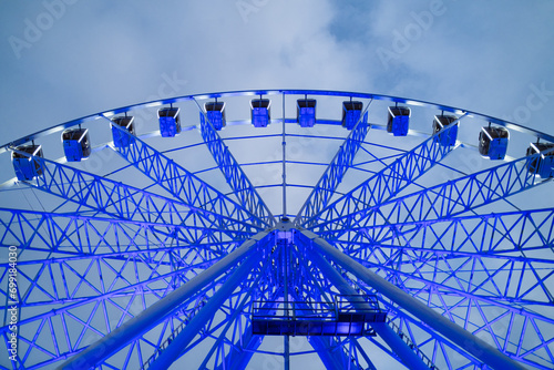 Underside view of colorful ferris wheel over evening sky at amusement park.