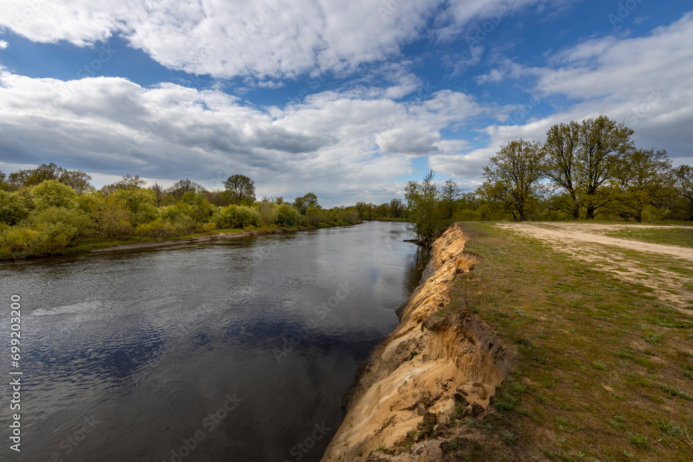 Spring landscape with a cliff near the river. Clouds over the horizon, young green trees along the river Spring landscape with a cliff near the river. Clouds over the horizon, young green trees along the river
