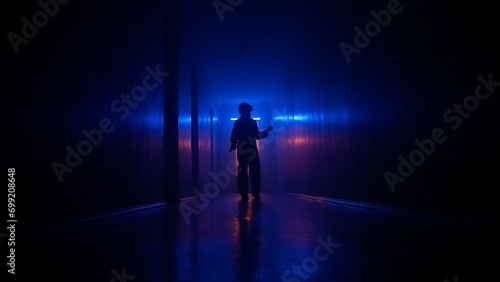 Portrait of silhouette in the hallway neon light. Person in chemical protection suit walking cautiously in the dark corridor  holding up to wall