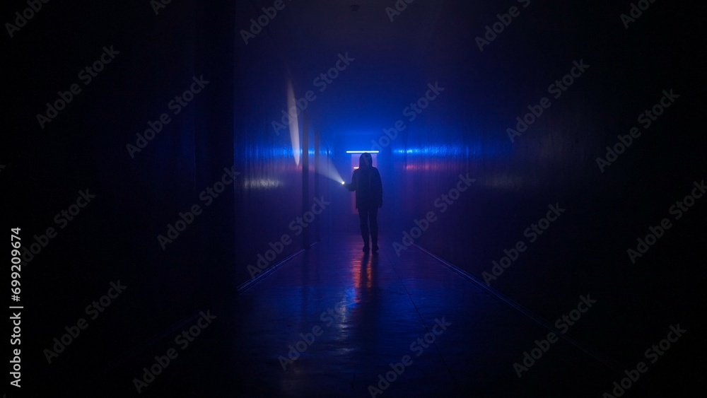 Portrait of female in the dark hallway with neon light. Woman with flashlight walking down the hallway in basement exploring it,