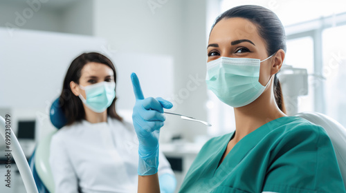 Healthcare professional in the foreground giving a thumbs-up and wearing a surgical mask  with a colleague in the background doing the same  both in a clinical setting.