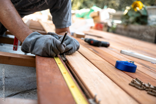 Worker with protective gloves marking a spot on wooden plank while placing it on a foundation for outside patio photo