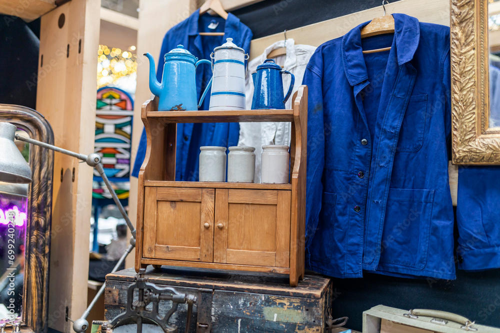 A blue jacket, white cans for bulk products on a small light chest of drawers from the seventies at an antique market. A blue jacket, white cans for bulk products on a small light chest of drawers from the seventies at an antique market.