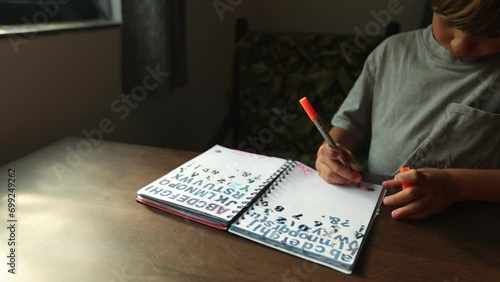 Young student diligently prints letters in his notebook, trying to make each line smooth and neat. 