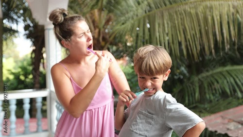 Mom and son diligently brush their teeth standing on hotel balcony in early morning. Dental care.