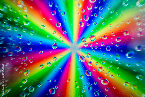 A radial burst of vibrant rainbow colors blurred behind a pattern of clear water droplets on a glass surface photo