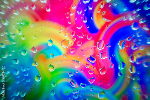 Glass surface with water droplets over a swirling, colorful abstract background with shades of the rainbow