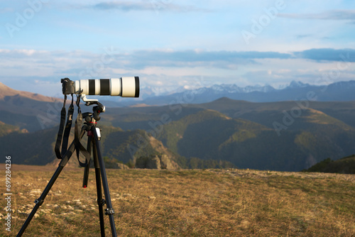 Photography of a distant object at long shutter speed. A camera with a long lens on a tripod against a mountainous terrain. Copy space.
