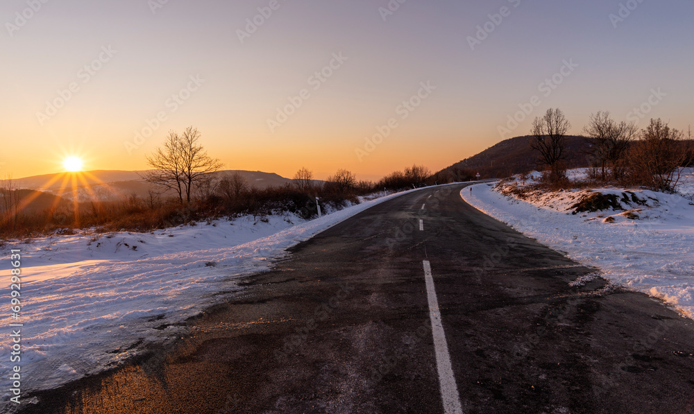 Empty asphalt road in rural landscape at sunset. Blue sky above the road. The sun's rays fall on the wet asphalt of the main road. Winter scene.