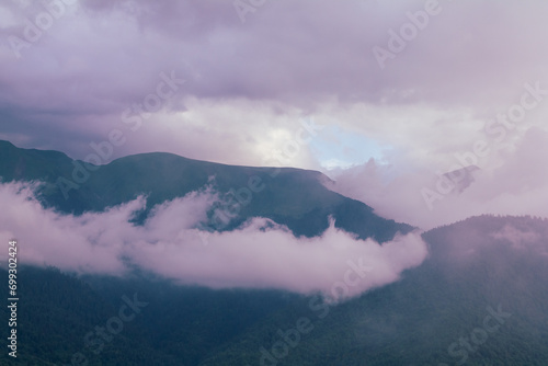 Fog and clouds in the mountains against the backdrop of the setting sun, changeable weather in the mountains, clouds and nebula on mountain peaks wide