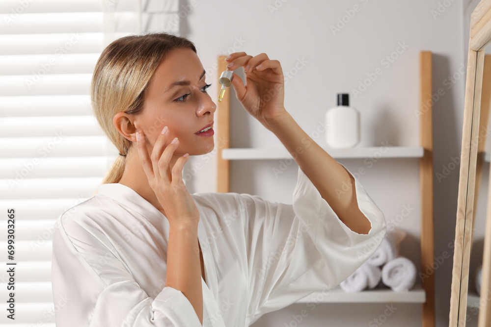 Beautiful woman applying cosmetic serum onto her face in bathroom Beautiful woman applying cosmetic serum onto her face in bathroom