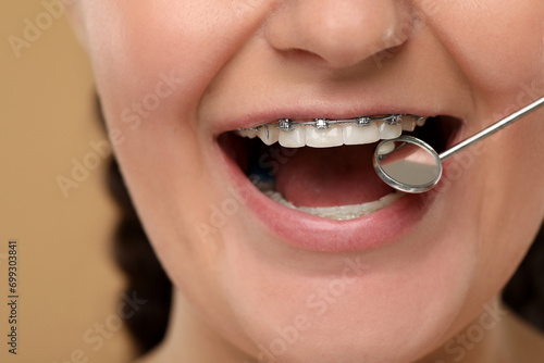 Examination of woman's teeth with braces using dental mirror on brown background, closeup
