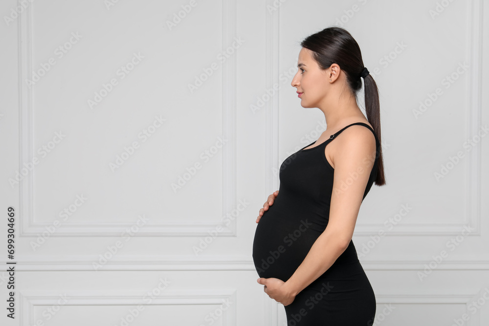 Beautiful pregnant woman in black dress near light grey wall, space for text Beautiful pregnant woman in black dress near light grey wall, space for text