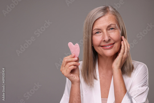 Woman with rose quartz gua sha tool on grey background, space for text. Facial massage photo