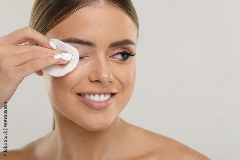 Beautiful woman removing makeup with cotton pad on light grey background, closeup. Space for text Beautiful woman removing makeup with cotton pad on light grey background, closeup. Space for text
