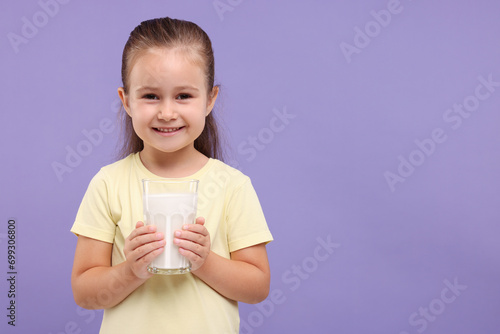 Cute girl with glass of fresh milk on violet background, space for text