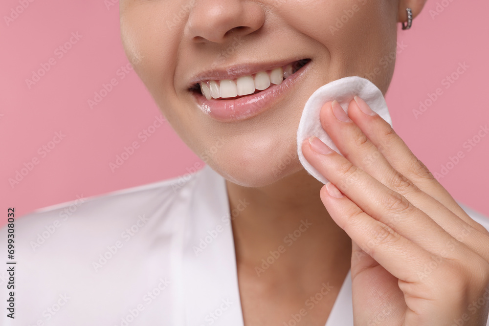 Young woman cleaning her face with cotton pad on pink background, closeup Young woman cleaning her face with cotton pad on pink background, closeup