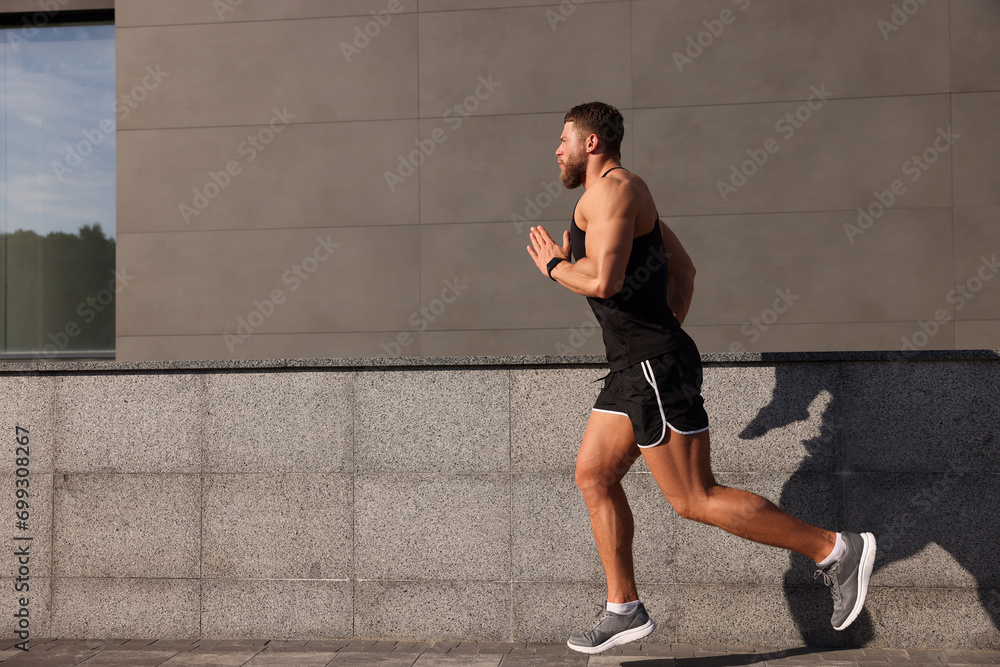 Fototapeta premium Young man running near building outdoors. Space for text