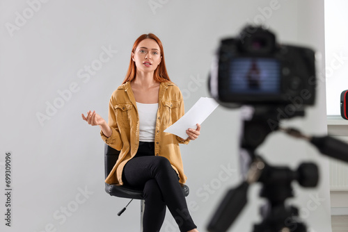 Casting call. Young woman with script performing in front of camera against light grey background at studio photo