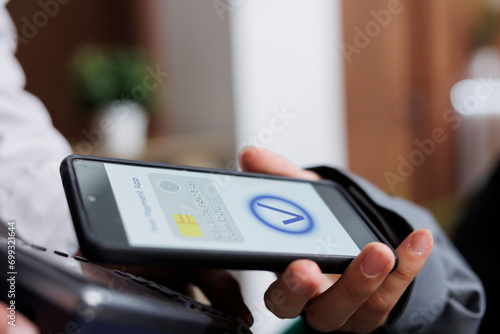 Close-up shot of tourist making contactless payment via mobile phone using NFC technology. Detailed view of pair of hands grasping pos terminal and smartphone, paying winter holiday reservation.