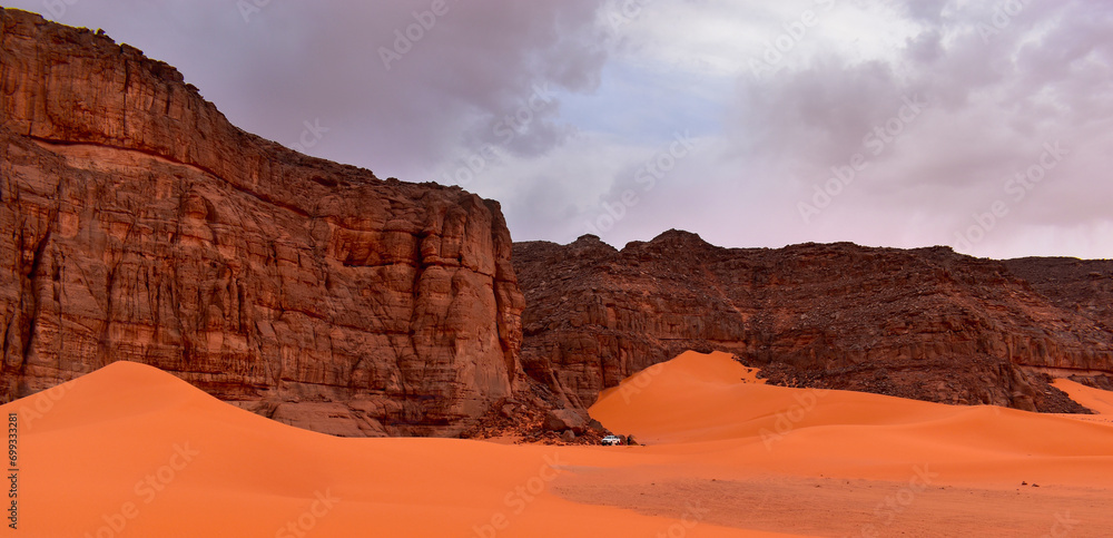 Camping in the Sahara, hiking in the desert by the rock. Sahara, orange dunes. Holidays and travel in Algeria, afternoon light over the desert. Rocks in the background.