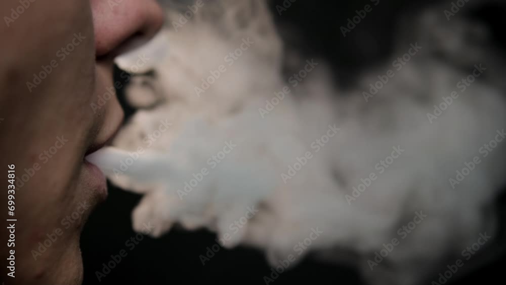 The guy smokes a vape. Close up on a black background. Nicotine addiction concept. Lips exhale smoke The guy smokes a vape. Close up on a black background. Nicotine addiction concept. Lips exhale smoke