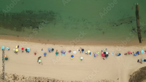 Aerial top down view bird eye view of beach in Nora (Pula), Sardinia, Italy. Beatiful coastline, colorful umbrellas and people swimming. 4K drone shot. photo