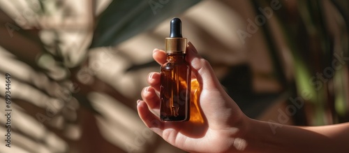 Women holding amber glass bottle with cosmetic serum on brown background. Mockup of container with dropper lid and collagen in sunlight. Skin care concept. photo