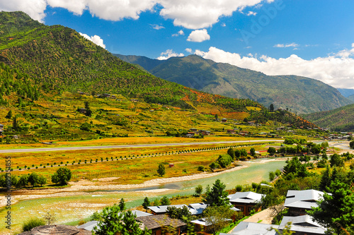 A panoramic view of the airport and the Paro Valley, Bhutan. Landscape with Mountain, river, green meadows and agricultural land, blue sky with white clouds.