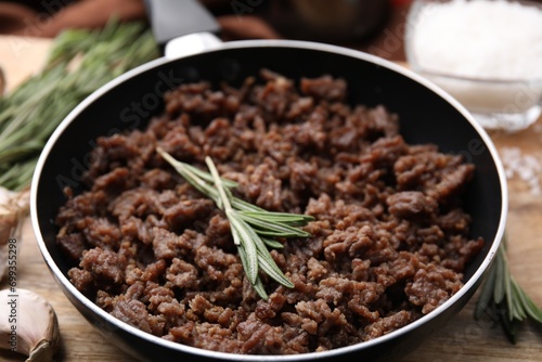 Fried ground meat in frying pan and rosemary on table, closeup