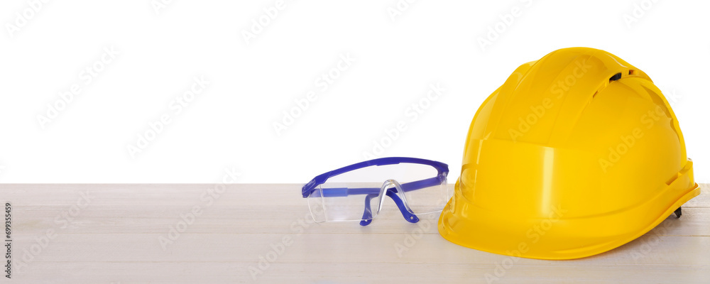 Hard hat and goggles on light wooden table against white background. Safety equipment Hard hat and goggles on light wooden table against white background. Safety equipment