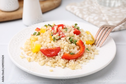 Plate of cooked bulgur with vegetables on white tiled table, closeup