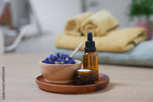Bottle of essential oil, dry flowers and jar with cream on light wooden table. Spa therapy