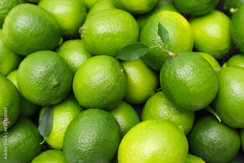 Many fresh limes with green leaves as background  top view