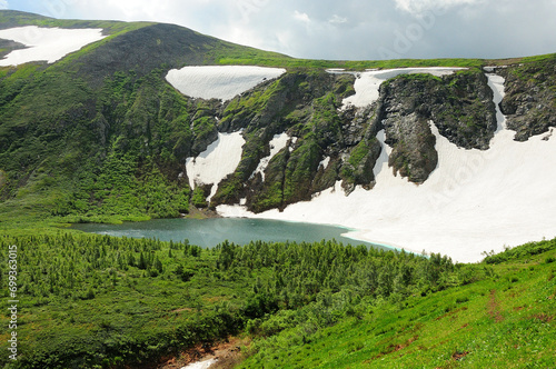 A path through low bushes to a beautiful lake in an intermountain basin at the foot of a hill with snow on the slopes.