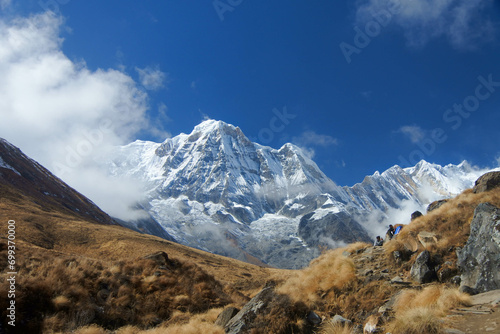 Stunning views of snow mountains, blue skies and large rocks along the track to Annapurna Base Camp.Keywords language: English
