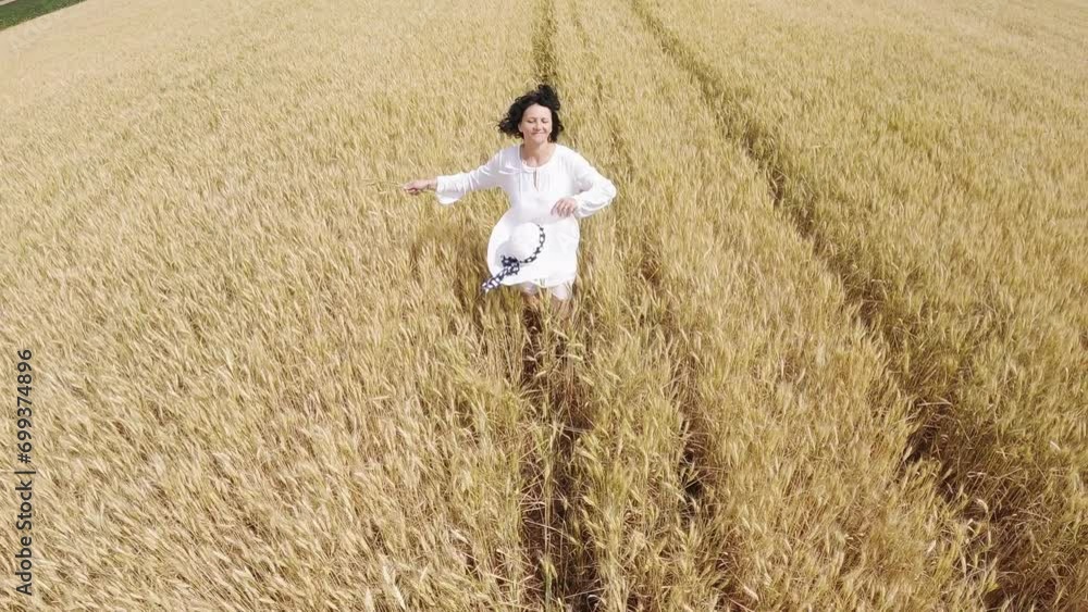 Agronomist carefree woman wearing hat and dress running across a yellow wheat field enjoying nature, slow motion . Agronomist carefree woman wearing hat and dress running across a yellow wheat field enjoying nature, slow motion .