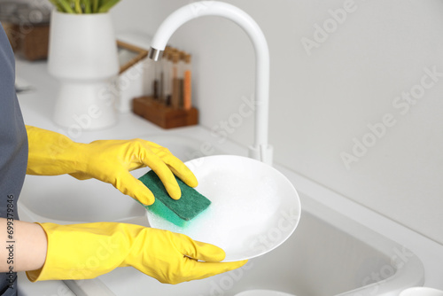 Woman in yellow rubber gloves washing plate with sponge in light kitchen photo
