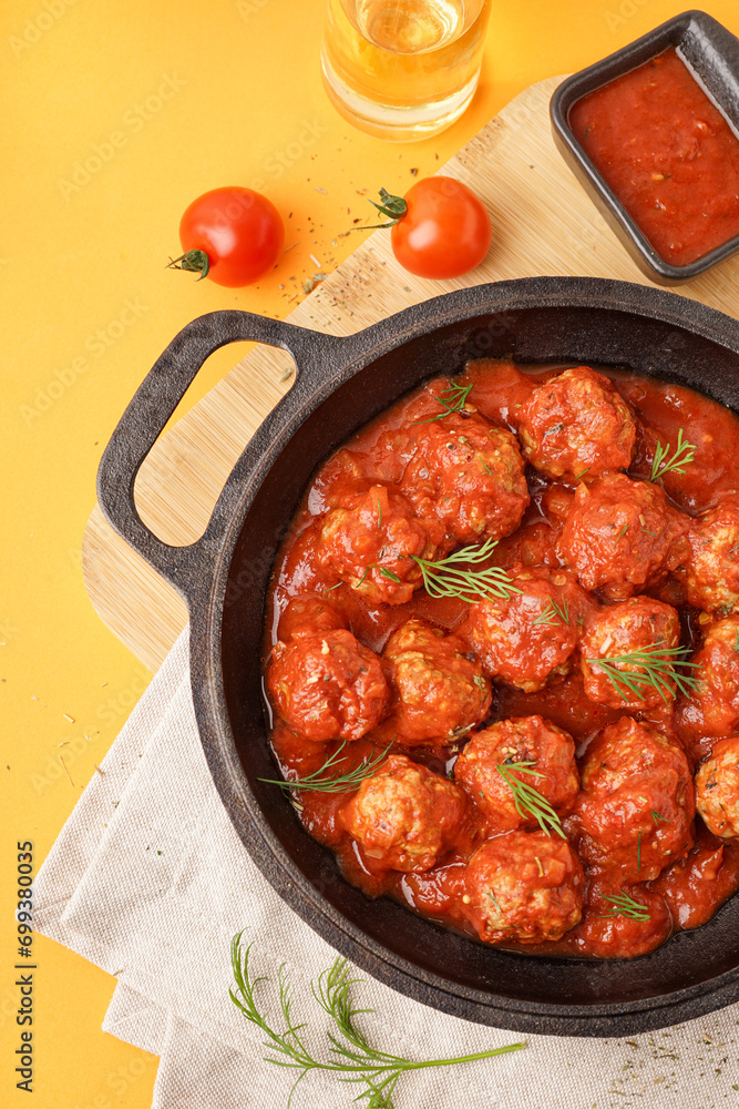 Frying pan of tasty meat balls with tomato sauce and dill on yellow background Frying pan of tasty meat balls with tomato sauce and dill on yellow background
