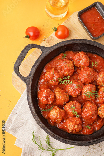 Frying pan of tasty meat balls with tomato sauce and dill on yellow background