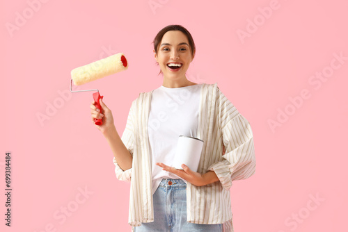 Young woman with paint roller and can on pink background photo