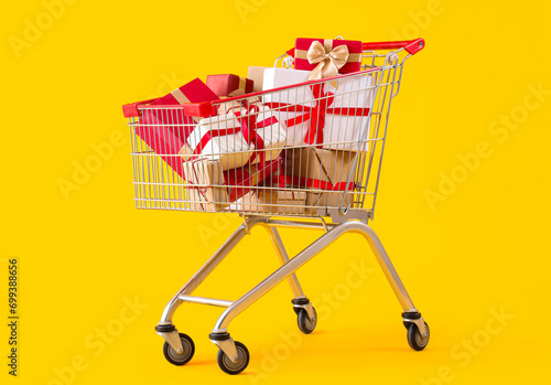 Shopping cart full of Christmas gift boxes on yellow background