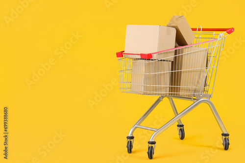 Shopping cart full of cardboard boxes on yellow background