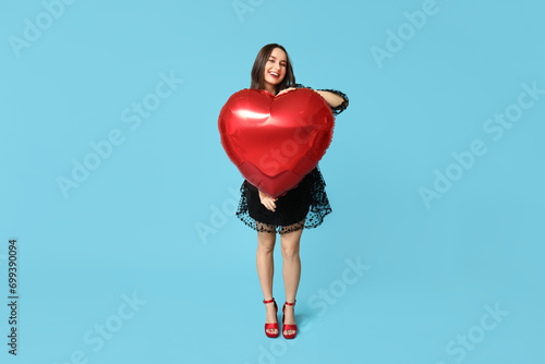 Beautiful young woman with heart shaped air balloon on blue background. Valentine's Day celebration