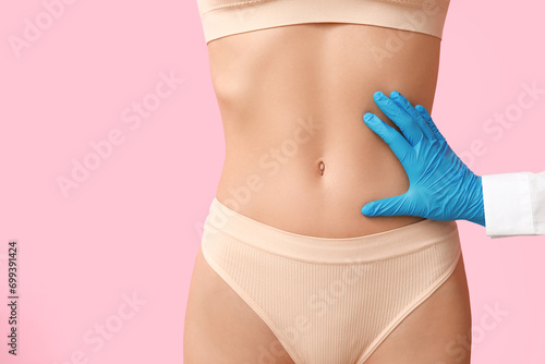 Young woman with flat belly and plastic surgeon on pink background, closeup