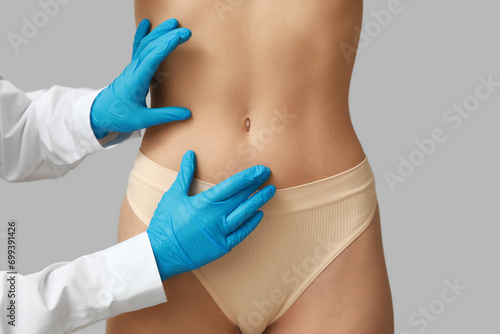 Young woman with flat belly and plastic surgeon on light background, closeup photo