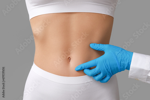 Young woman with flat belly and plastic surgeon on light background, closeup
