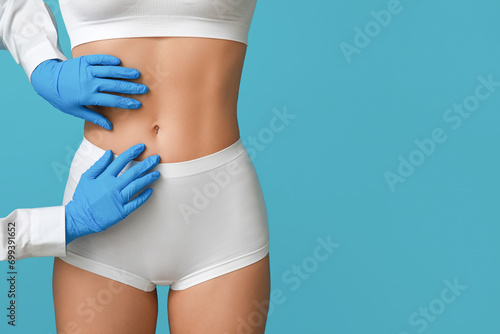 Young woman with flat belly and plastic surgeon on blue background, closeup photo