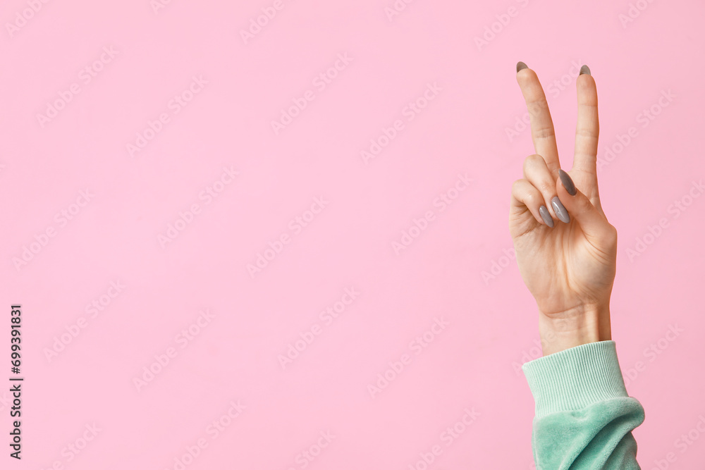 Young woman showing peace sign on pink background