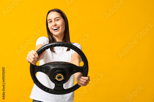 Beautiful young woman with steering wheel on yellow background